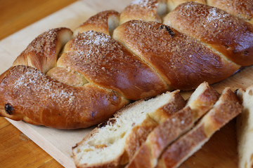 Appetizing baked sweet bun with raisins in the form of a pigtail with sugar on a wooden board.