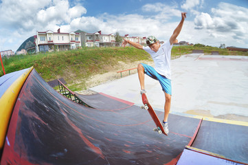 A teenager in shorts and a cap does an allie stunt on a ramp in a skate park in a residential area...