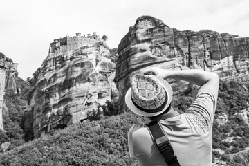 Rear view of a male photographer photographing the blurred Holy Monastery of Varlaam, part of the Eastern Orthodox monastery complex of Meteora, Greece, black and white photography