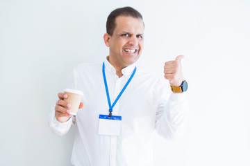 Middle age business man wearing ID card and drinking coffeeover white background pointing and showing with thumb up to the side with happy face smiling