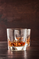 Two glasses of whisky with ice on a wooden table.