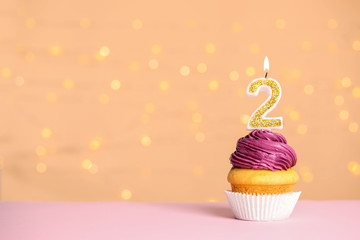 Birthday cupcake with number two candle on table against festive lights, space for text