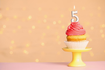 Birthday cupcake with number five candle on stand against festive lights, space for text