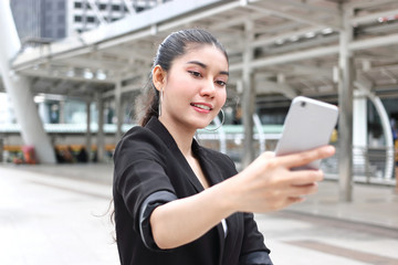 Attractive young Asian woman taking a photo or selfie with mobile smart phone on street of modern city.