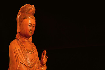 Buddhist religion and meditation. Kannon of Guanyin, the Goddess of Mercy, wooden statuette on black background (with copy space)