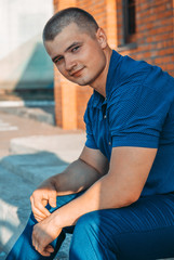 Young handsome sporty man in a blue business suit on a background of a brick wall in the summer.