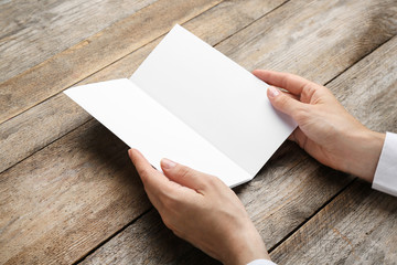 Obraz premium Young woman holding blank brochure at wooden table, closeup. Mock up for design
