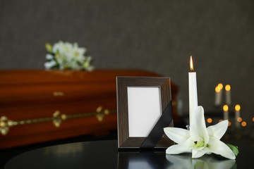 Black photo frame with burning candle and white lily on table in funeral home
