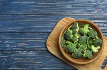 Bowl of fresh broccoli on blue wooden table, top view with space for text