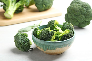 Bowl and fresh broccoli on light grey table