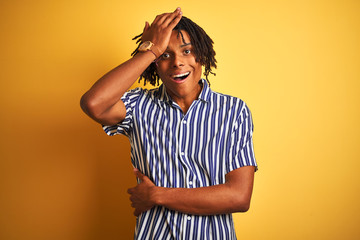 Afro man with dreadlocks wearing casual striped t-shirt over isolated yellow background surprised with hand on head for mistake, remember error. Forgot, bad memory concept.