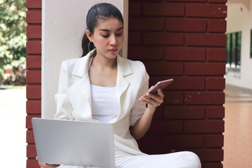 Attractive young Asian business woman working with laptop and mobile smart phone at outside office.