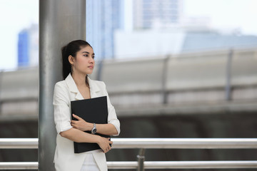 Stressed young Asian business woman with document folder standing at outside office.