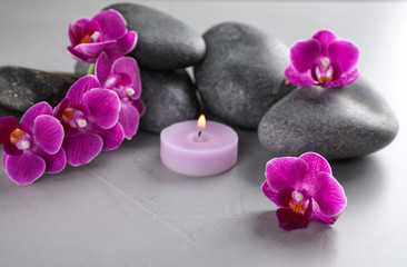 Spa stones, orchid flowers and candle on grey table