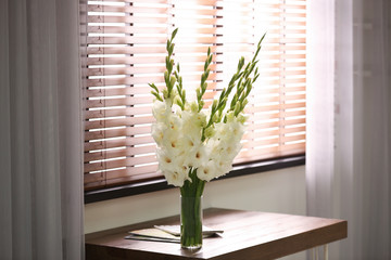 Vase with beautiful white gladiolus flowers on wooden table in room, space for text
