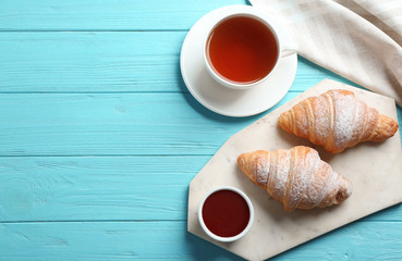 Marble board with tasty croissants, cup of tea and space for text on light blue wooden background, flat lay. French pastry