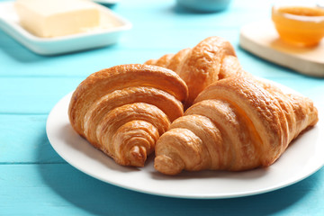 Plate with tasty croissants on light blue wooden table, closeup. French pastry