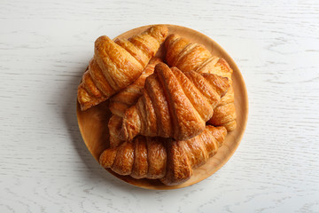 Plate with tasty croissants on white wooden background, top view. French pastry