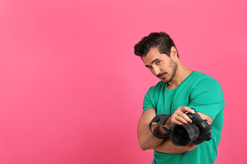 Young photographer with professional camera on pink background. Space for text