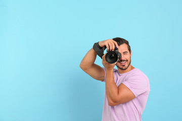 Young professional photographer taking picture on light blue background. Space for text - obrazy, fototapety, plakaty