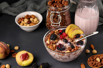 Granola crispy honey muesli with natural yogurt, fresh berries and fruit, chocolate and nuts in a glass bowl against a dark background, healthy food, horizontal orientation