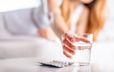 Suffering sick woman in bed taking pills and glass of water