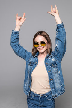 Full length portrait of a young woman showing rock gesture with hands isolated over gray background.