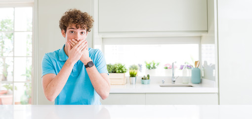 Wide shot of young handsome man at home shocked covering mouth with hands for mistake. Secret concept.