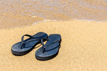 Fototapeta na wymiar A pair of flip flops (Thongs), on an Hawaiian shoreline, with the sea lapping close to the shoes