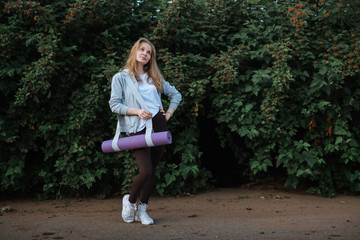 Fitness woman carrying yoga mat with strap on vegetative background
