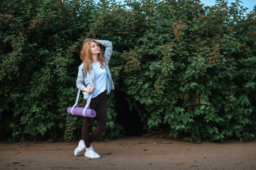 Fitness woman carrying yoga mat with strap on vegetative background