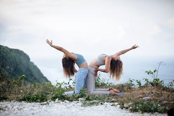 Pair of girls practice yoga against the background of the ocean