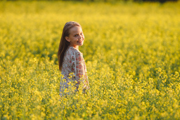 Fototapeta premium The concept of health and youth. Carefree young girl enjoys the sunset in a canola field.