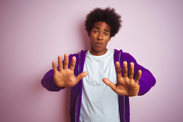 Young african american man wearing purple sweatshirt standing over isolated pink background Moving...
