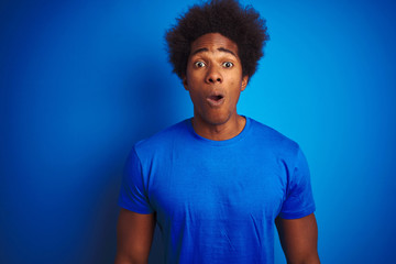 Fototapeta na wymiar African american man with afro hair wearing t-shirt standing over isolated blue background afraid and shocked with surprise expression, fear and excited face.