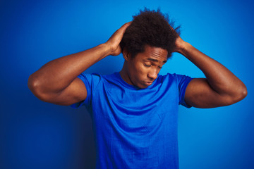 Fototapeta na wymiar African american man with afro hair wearing t-shirt standing over isolated blue background suffering from headache desperate and stressed because pain and migraine. Hands on head.