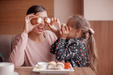 Funny mom with daughter holding sushi rolls in front of eyes
