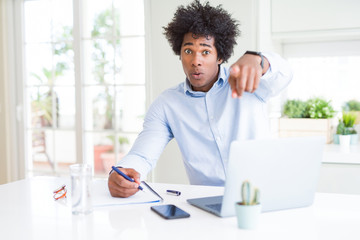 African American business man working writing on notebook pointing with finger to the camera and to you, hand sign, positive and confident gesture from the front