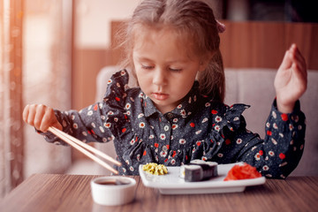 Cute little girl eating sushi in the cafe
