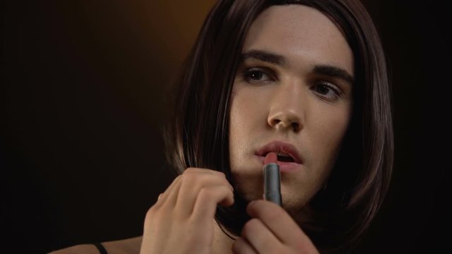Beautiful transgender man applying lipstick, feels comfortable in female makeup