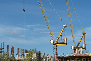 Naklejka premium Two construction cranes at a construction site. Tall crane on a blue sky. The construction of a multi-storey.
