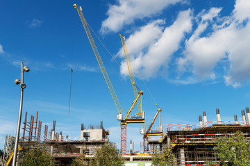 Two construction cranes on a building construction. High crane on a blue sky with clouds. The construction of a multi-storey.