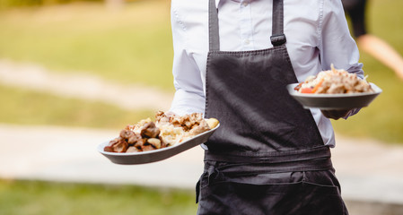 Catering service. Waiter man in apron carries food snacks on platter