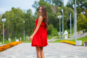 Young beautiful girl in red dress walking on the summer street