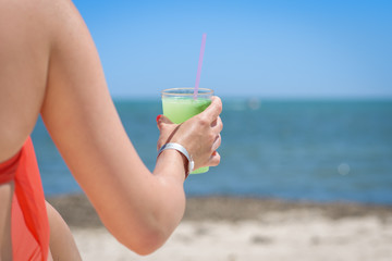 Young European lady is sitting at sunbed near sea. She is enjoying her holidays and holding glass of cocktail in her hands.