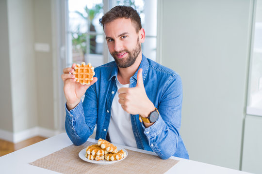 Handsome man eating sweet Belgian pancakes happy with big smile doing ok sign, thumb up with fingers, excellent sign