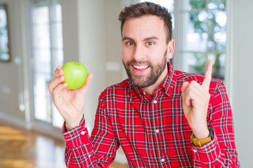 Handsome man eating fresh healthy green apple very happy pointing with hand and finger to the side