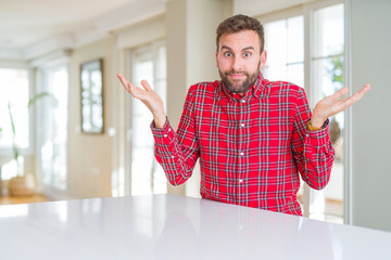 Handsome man wearing colorful shirt clueless and confused expression with arms and hands raised....
