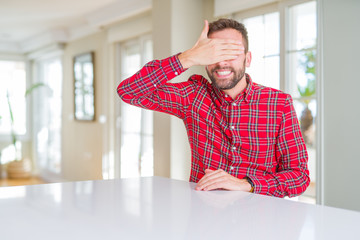 Fototapeta premium Handsome man wearing colorful shirt smiling and laughing with hand on face covering eyes for surprise. Blind concept.