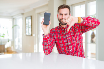 Handsome man showing smartphone screen with angry face, negative sign showing dislike with thumbs...